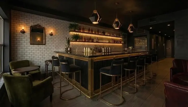 Softly lit bar with brass stools and shelves of non-alcoholic spirits inside The Sober Bar in Gulfport, Florida