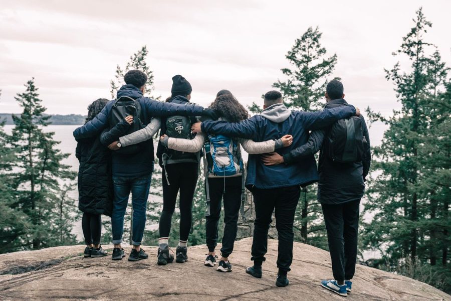 Six friends with arms around each other looking out from a forest clifftop