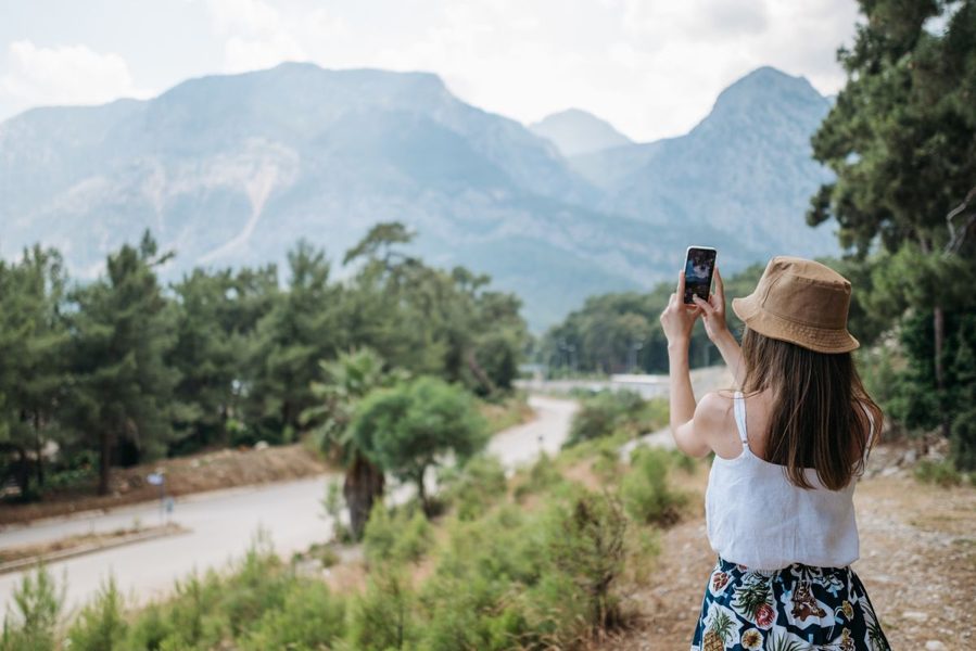 Traveler in a straw hat photographing a mountain landscape with her phone